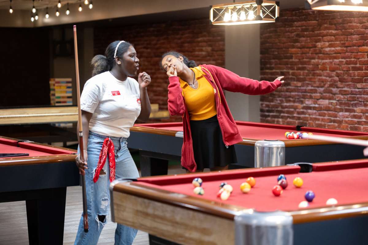 Two students singing next to a pool table